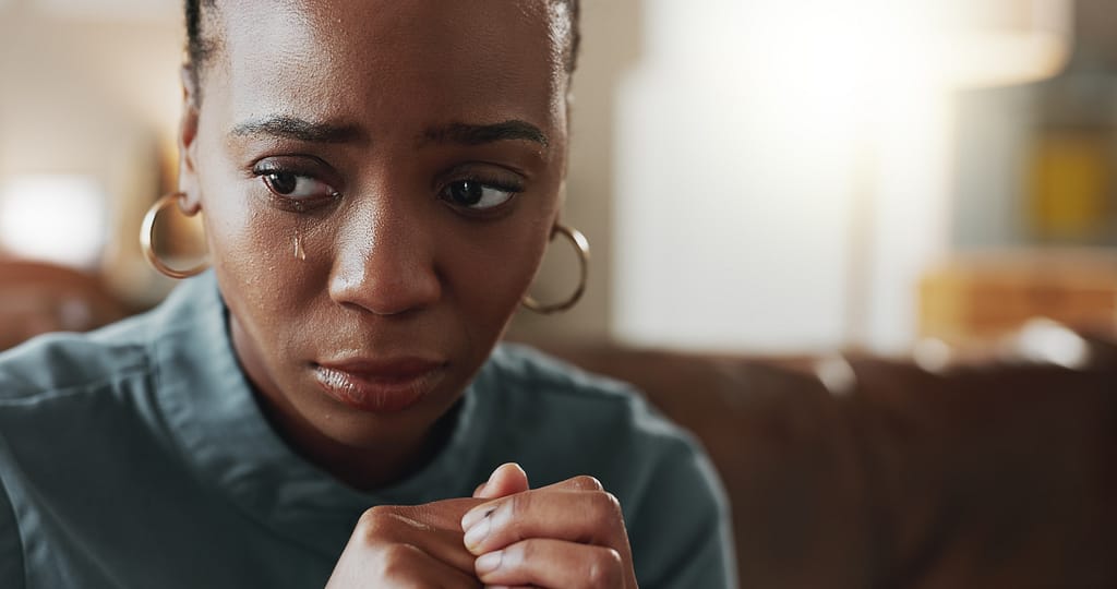 Crying, sad and black woman with depression, thinking or psychological trauma in home living room.
